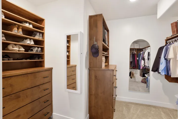 Built-in closet system featuring warm wood cabinetry, integrated shelving, an arched doorway, and carpeted flooring