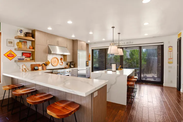 Spacious kitchen featuring an extended white countertop island, integrated stainless steel appliances, upper and lower wood-finish cabinetry, recessed ceiling lighting, and dark wood-finish flooring