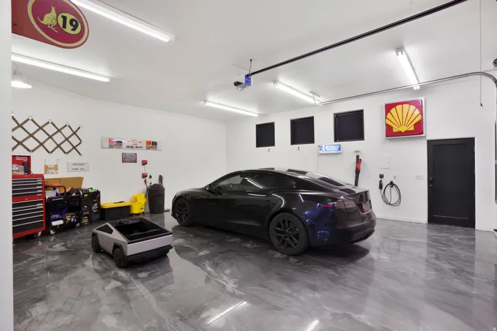 Spacious garage featuring a durable epoxy floor finish, abundant overhead fluorescent lighting, and multiple wall-mounted power outlets