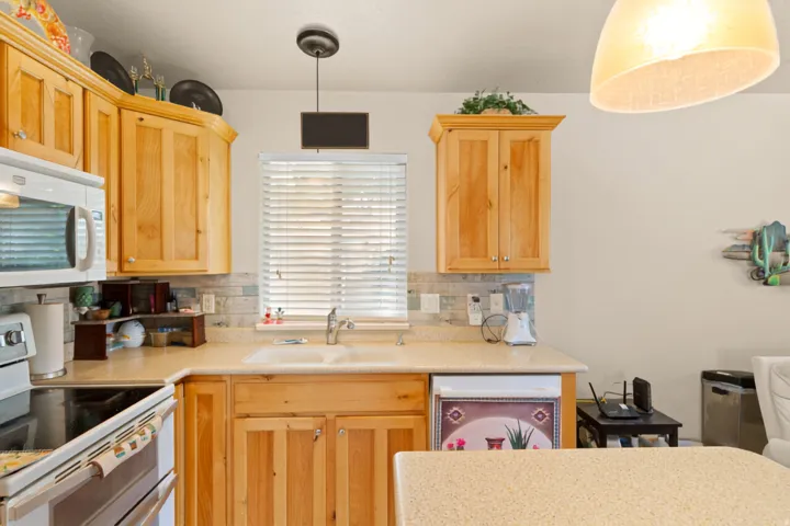 Kitchen featuring light wood cabinetry, light-toned countertops, a stainless steel microwave, a built-in dishwasher, and a tile backsplash