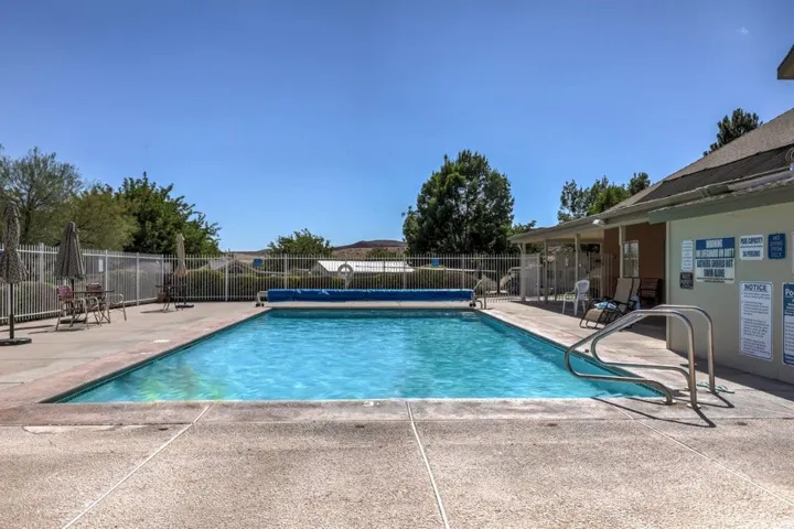 Rectangular swimming pool with a concrete surround, metal perimeter fencing, and an adjacent building