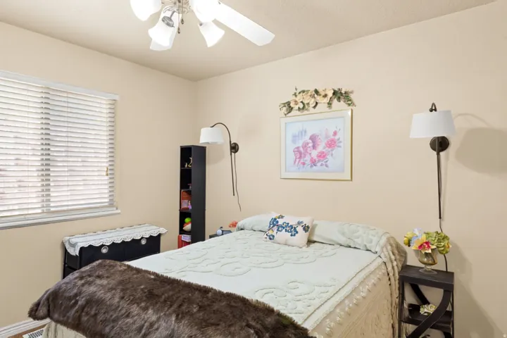 Window with blinds, ceiling fan with light fixture, and wall-mounted sconces