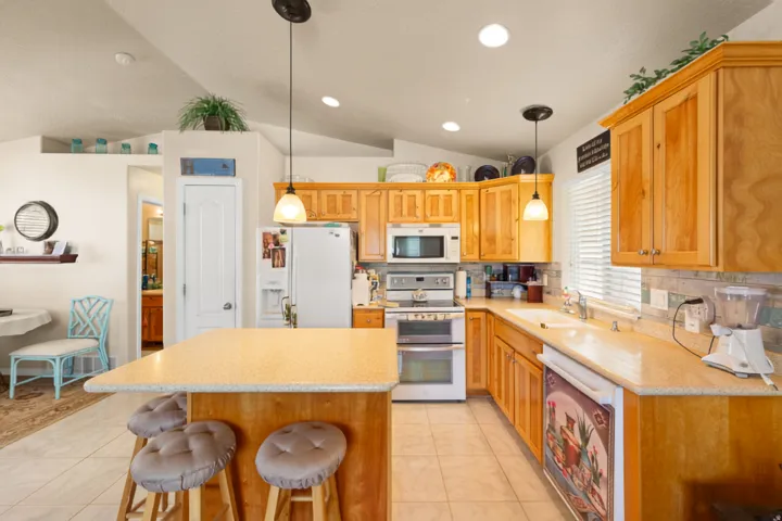 Kitchen featuring a vaulted ceiling, wood cabinetry, built-in stainless steel appliances, a kitchen island with seating, and tile flooring