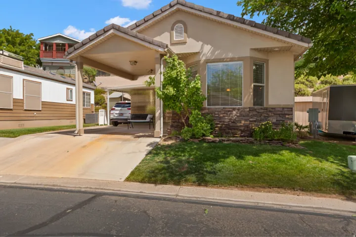 Stucco exterior with a stone veneer accent, bay window with blinds, covered carport, concrete driveway, and manicured lawn