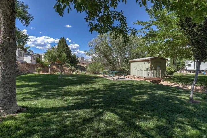 Expansive green space featuring a shed with a small deck, a paved patio area, and mature trees providing shade
