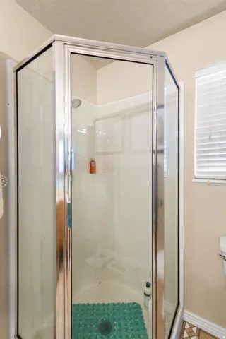 Corner glass-enclosed shower with a chrome frame and a built-in shelf