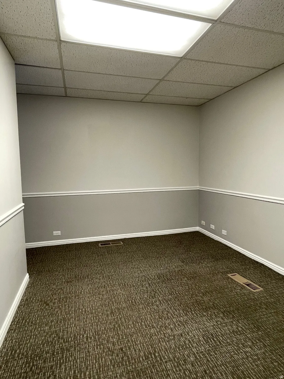 Carpeted interior space featuring neutral two-tone walls with chair rail molding and white baseboards