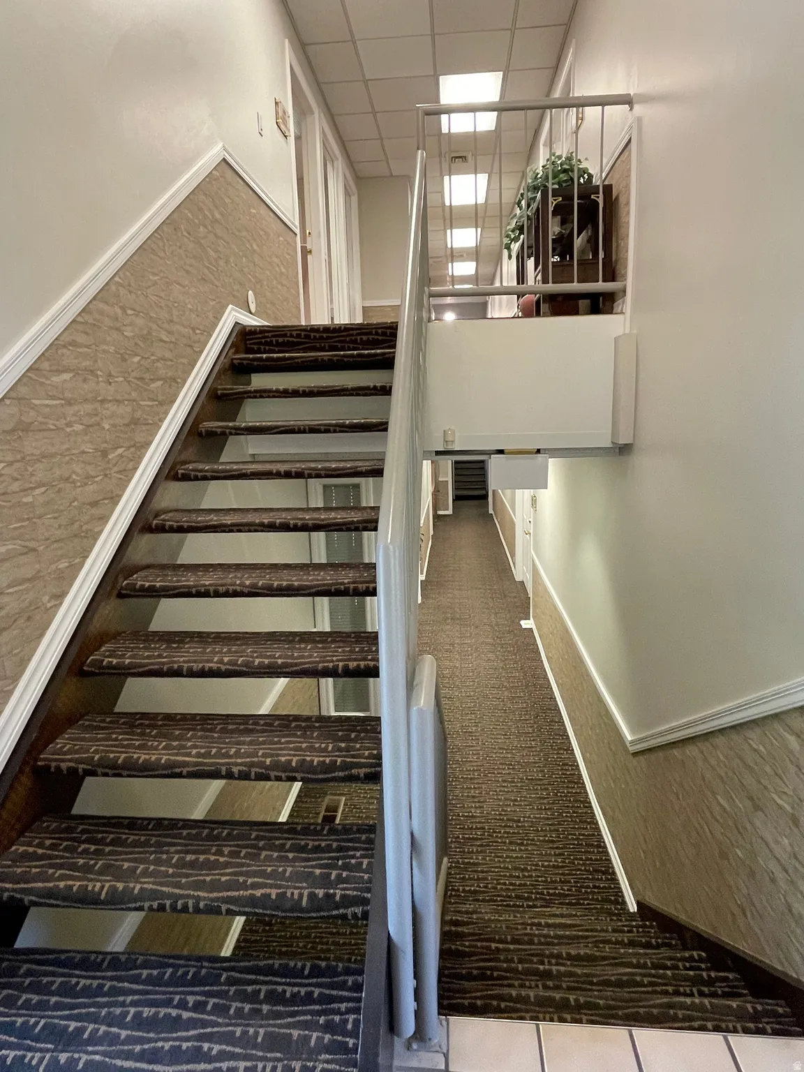 Staircase featuring patterned carpet treads and metal railing