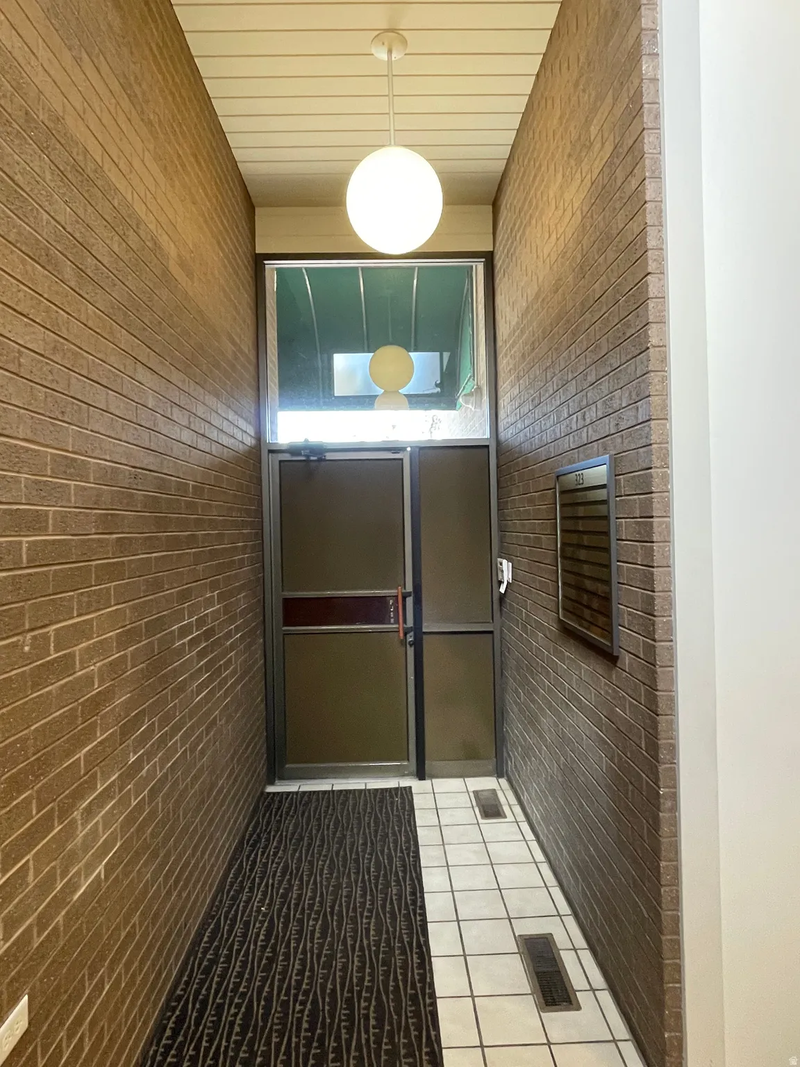 Brick-lined entryway featuring a glass-paneled door, transom window, and an overhead globe pendant light