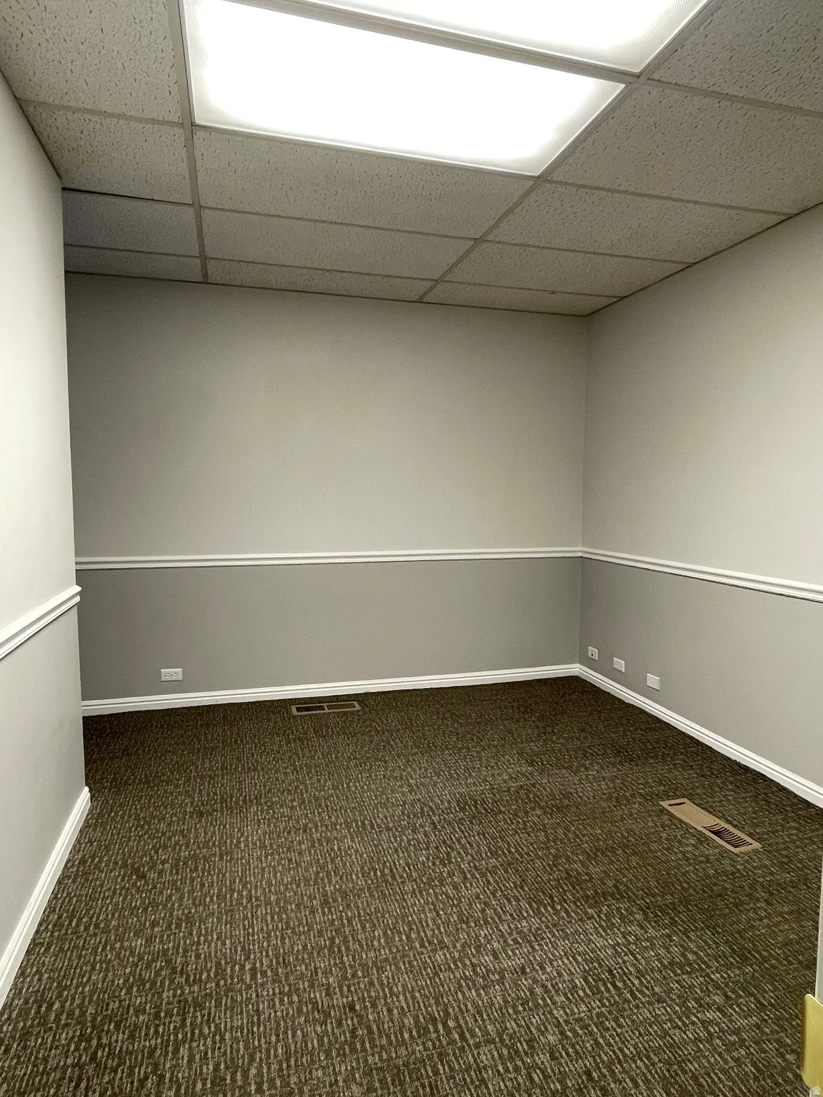 Spacious interior featuring a drop ceiling with recessed lighting, two-tone painted walls with chair rail and baseboard molding, and patterned carpet flooring
