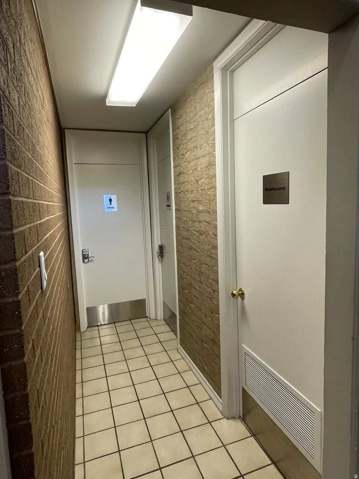 Corridor featuring brick-textured wall covering, a contrasting textured wall, and white tile flooring