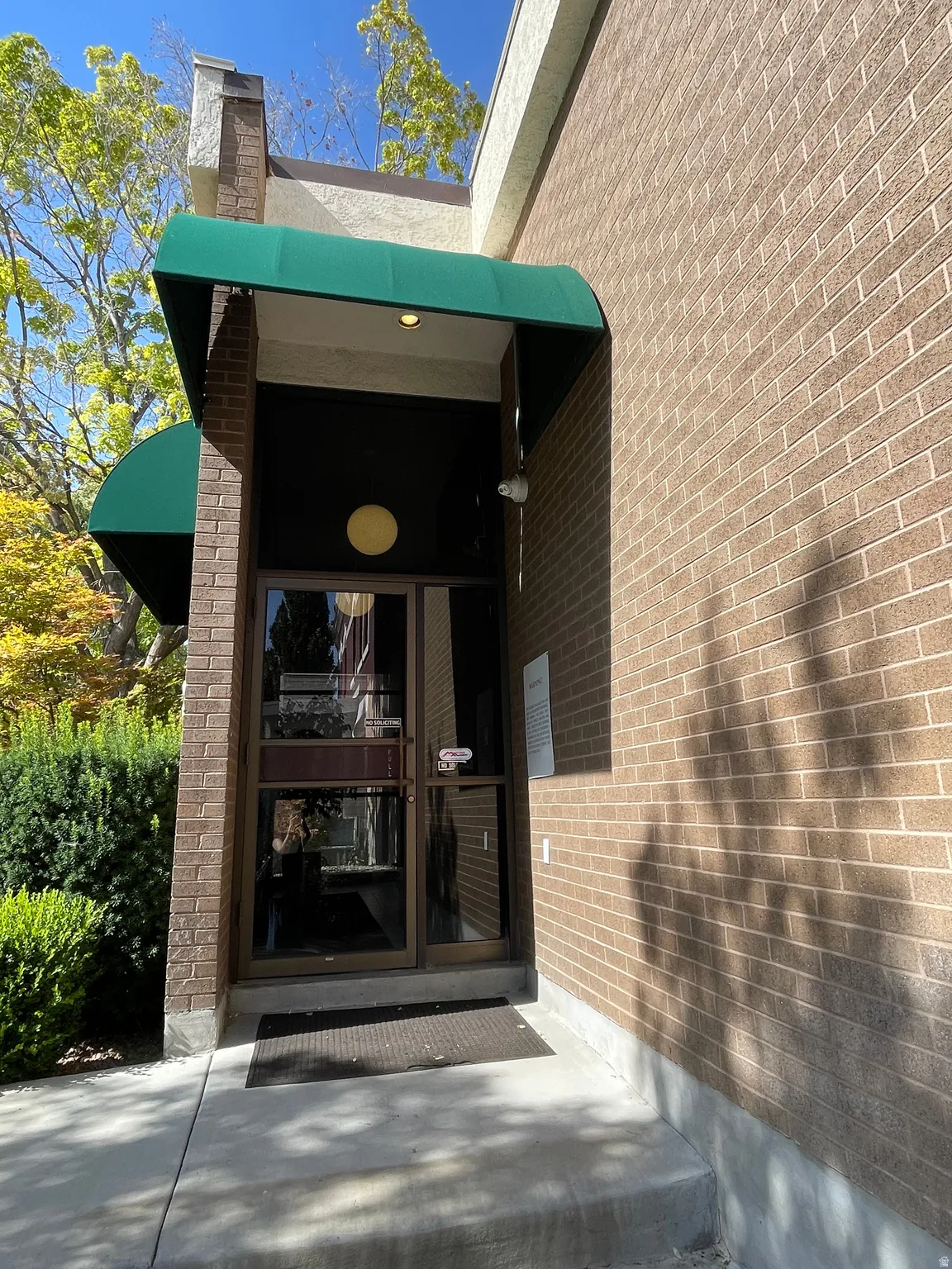 Entryway featuring a green fabric awning, brick facade, recessed lighting, double glass doors, and concrete steps