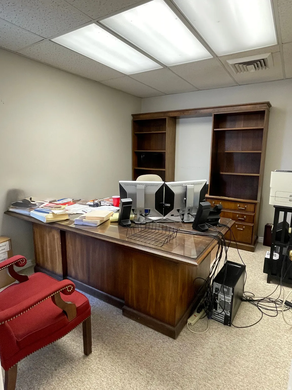 Office space featuring built-in wood-finish shelving, textured wall-to-wall carpeting, and recessed ceiling lighting with acoustic tile