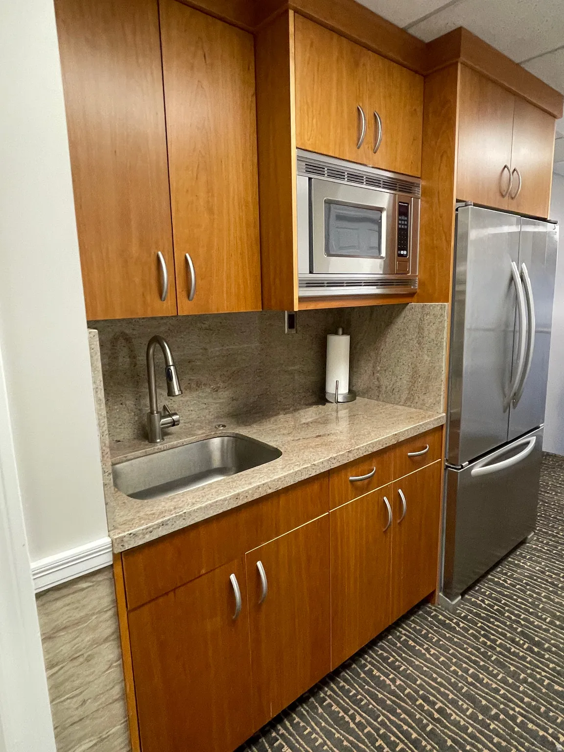 Compact kitchen area featuring wood-finish cabinetry, a stainless steel sink, and a microwave