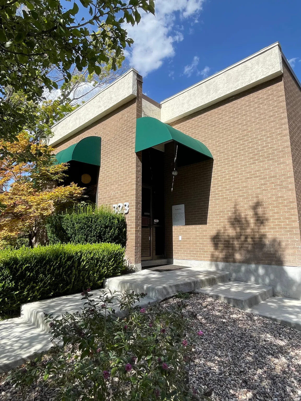 Brick exterior featuring green awnings, concrete steps, and established landscaping