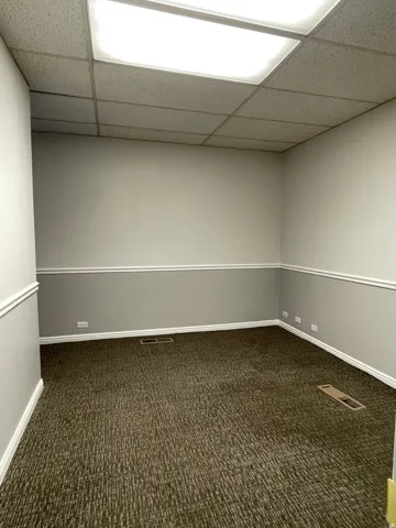 Spacious interior featuring a drop ceiling with recessed lighting, two-tone painted walls with chair rail and baseboard molding, and patterned carpet flooring