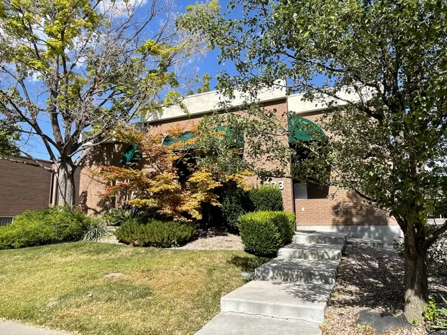 Brick facade building with arched green awnings, mature trees, and a concrete pathway