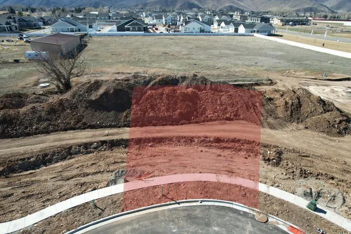 Graded building lot featuring a completed street with sidewalk and curb, surrounded by undeveloped land