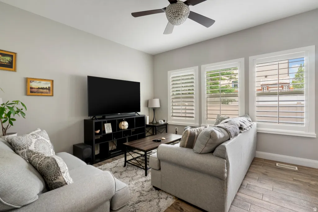 Living area featuring light gray wall tones, three large windows with white louvered shutters, and a modern ceiling fan with an integrated light fixture