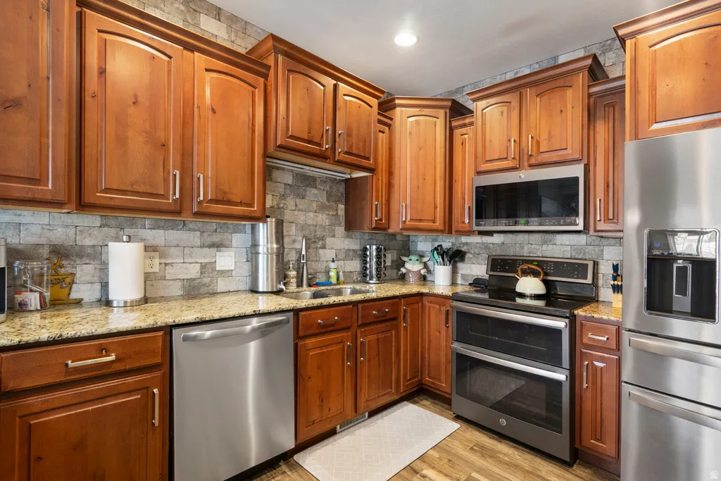 Kitchen featuring wood-finish cabinetry, light-colored granite countertops, and a stone-look tile backsplash