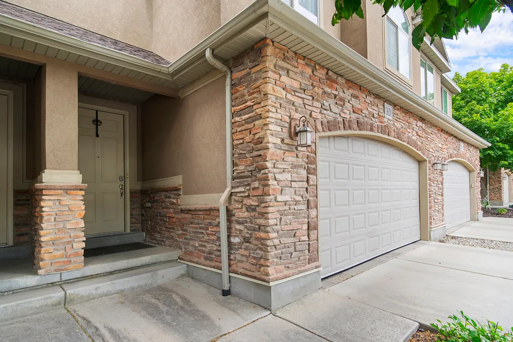 Stucco and stone veneer exterior featuring an arched garage door, concrete driveway, and an entryway with a covered porch