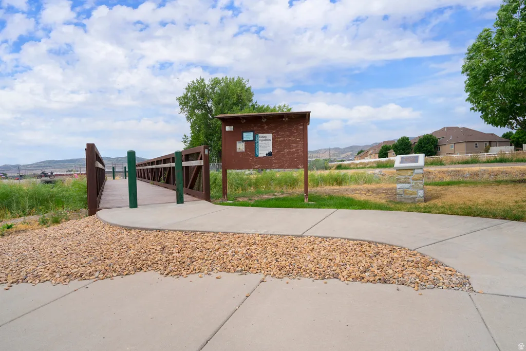 Paved pathway leading to a pedestrian bridge with brown railings and green posts, bordered by decorative gravel