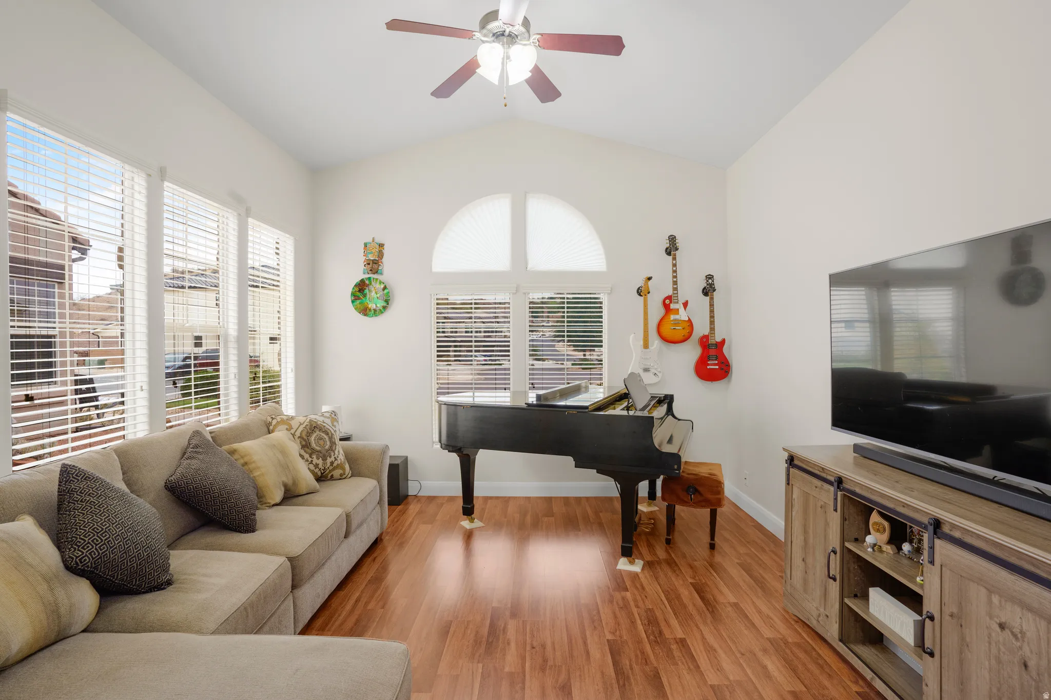 Vaulted ceiling living space with wood-finish flooring, multiple large windows, and a ceiling fan