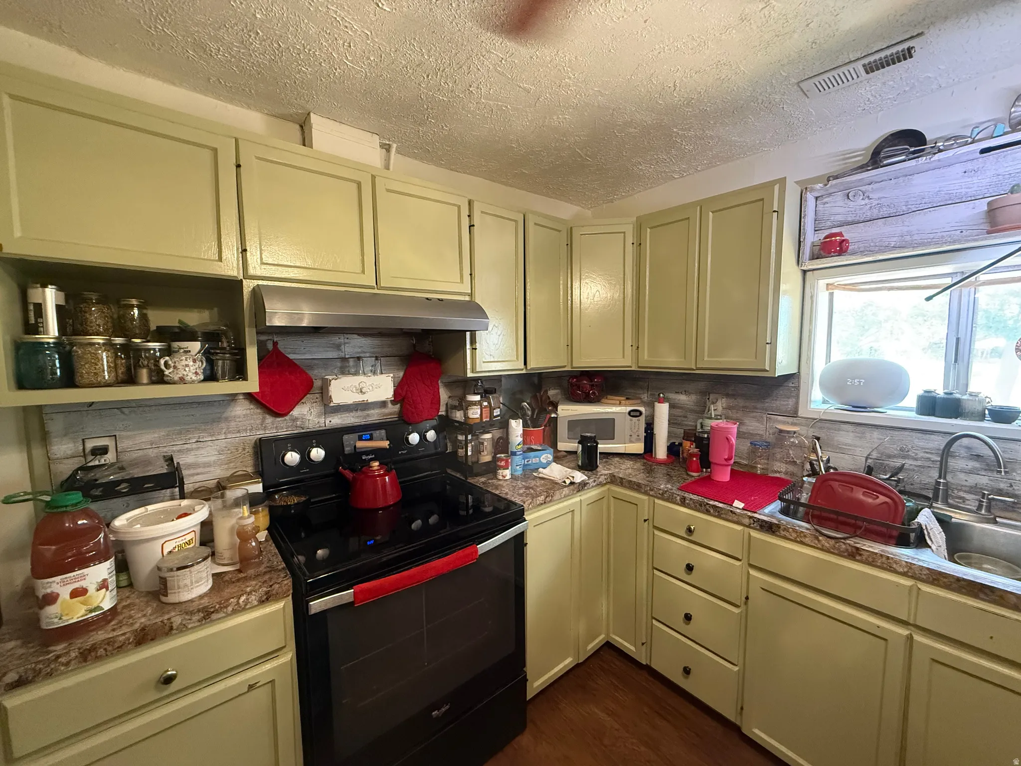 Kitchen featuring light-toned cabinetry, laminate countertops, a stainless steel sink, and a black range with an overhead exhaust fan