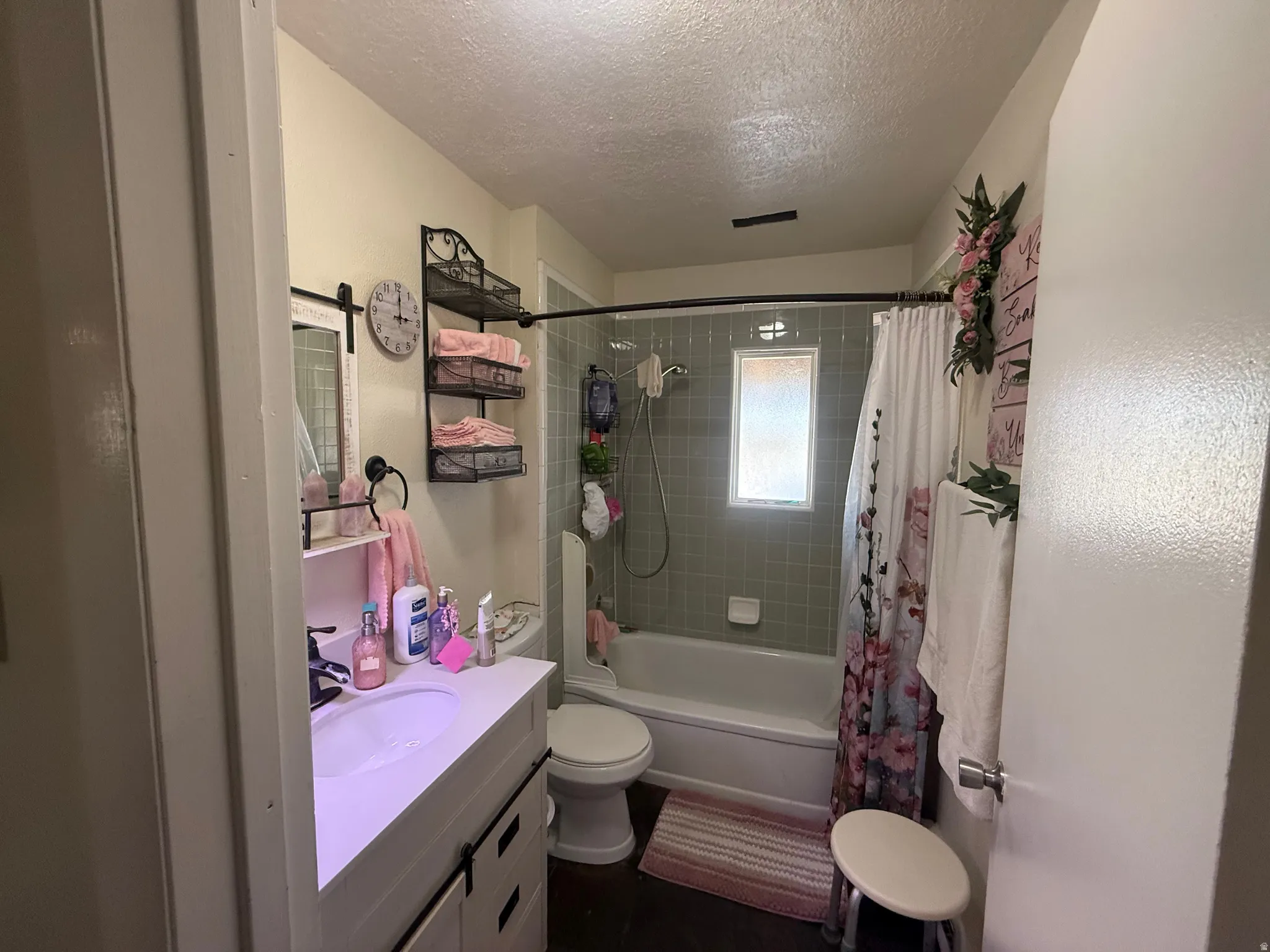 Bathroom featuring a white vanity with an integrated sink, a built-in tub with light green tile surround, and a frosted window