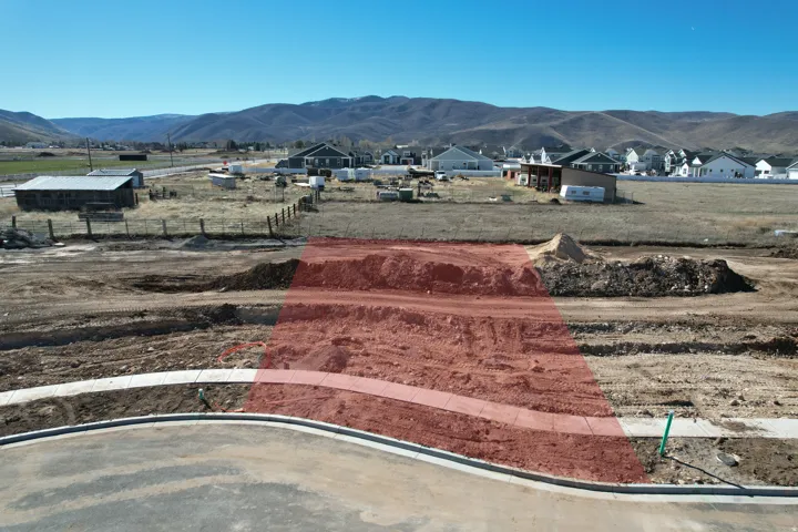 Developable land lot featuring a paved road, concrete sidewalk, and mountain backdrop