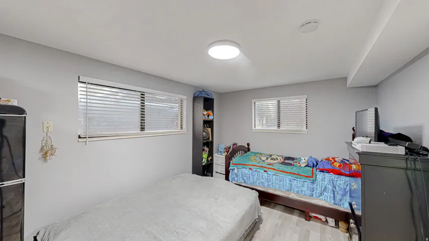 Room featuring two windows with horizontal blinds, light-toned wood-finish flooring, and a flush-mount ceiling light fixture