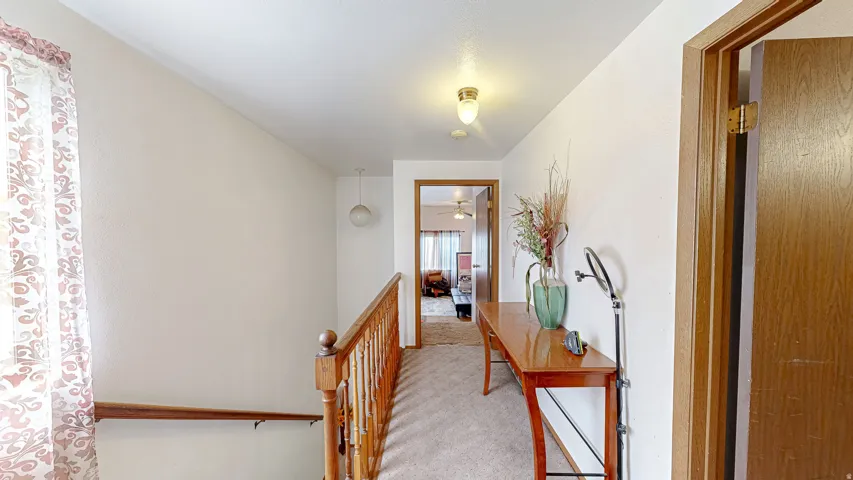 Carpeted hallway featuring a wooden banister, overhead lighting, and wood-finish doors