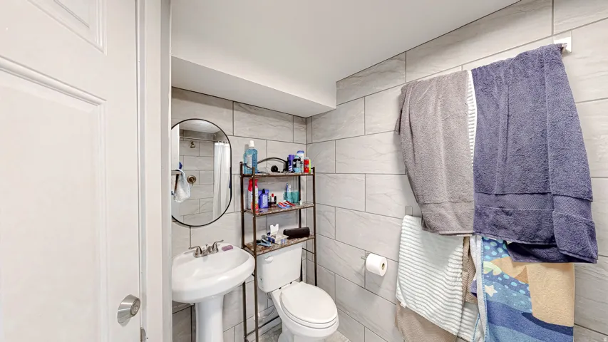 Bathroom featuring a pedestal sink with a chrome faucet, oval mirror, and tiled walls extending to the ceiling
