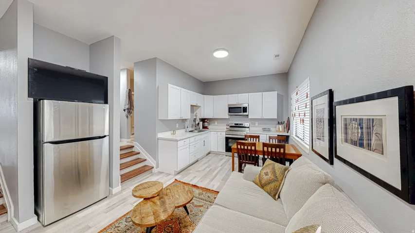 Open-concept living space with light wood-finish flooring, white cabinetry, stainless steel appliances, and a dining area