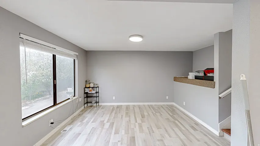 Spacious room featuring wood-finish flooring, a large window with blinds, and light gray painted walls