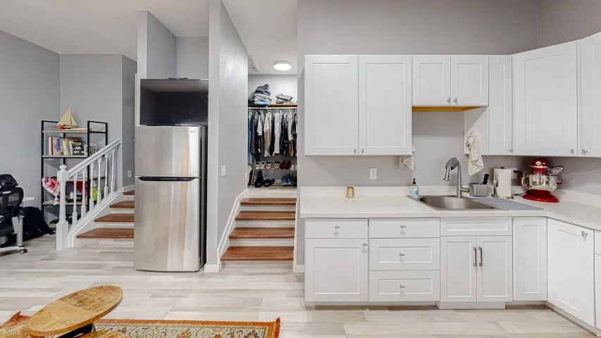 White cabinetry with satin nickel hardware and a stainless steel sink, complemented by light-toned countertops