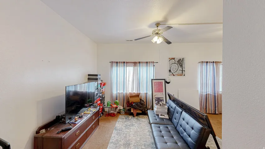 Living area featuring a ceiling fan with integrated lighting, multiple windows, and light-toned walls