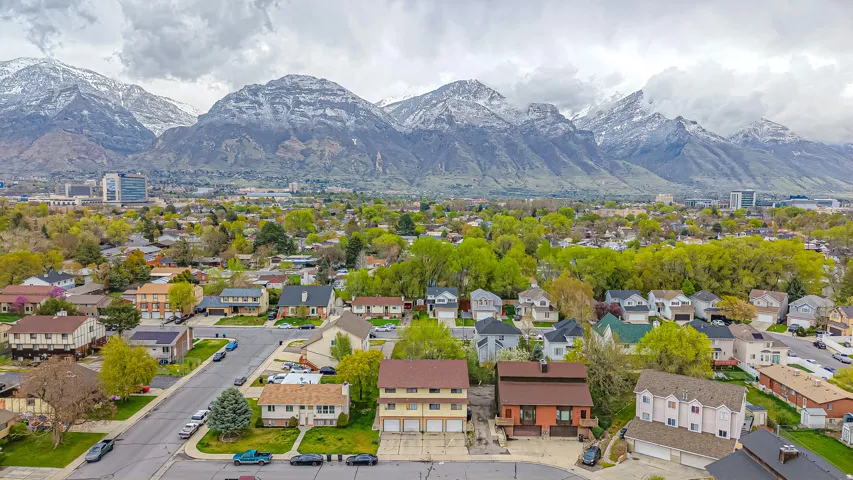 Residential area with varied architectural styles and mature trees against a backdrop of snow-capped mountains