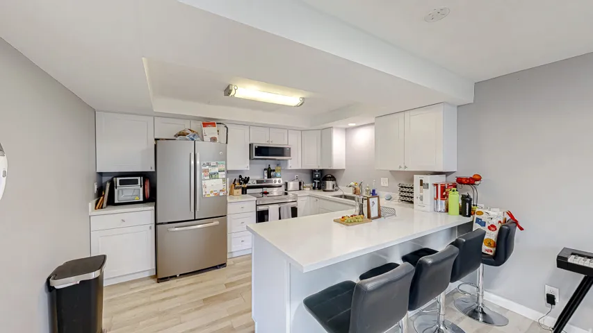 Modern kitchen featuring white cabinetry, stainless steel appliances, light-toned wood-finish flooring, and a peninsula with countertop seating
