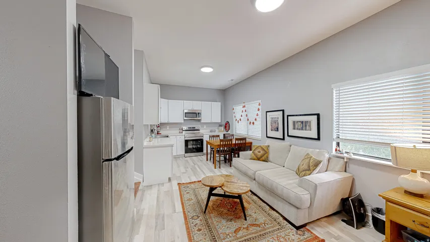 Open-concept living space featuring wood-finish flooring, recessed lighting, and a kitchen with white cabinetry and stainless steel appliances