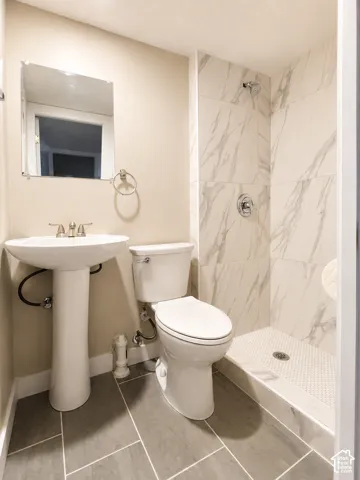 Bathroom featuring a pedestal sink, a toilet, a shower with a tiled surround, and grey rectangular floor tiles