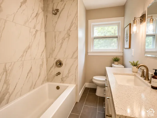Bathroom featuring a tub/shower combination with white marble-patterned tile surround, a built-in white bathtub, and brushed brass fixtures