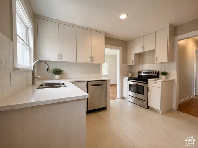 Modern kitchen featuring light-toned custom cabinetry and counters with brushed nickel hardware, light-colored countertops, stainless steel appliances, and a tile backsplash