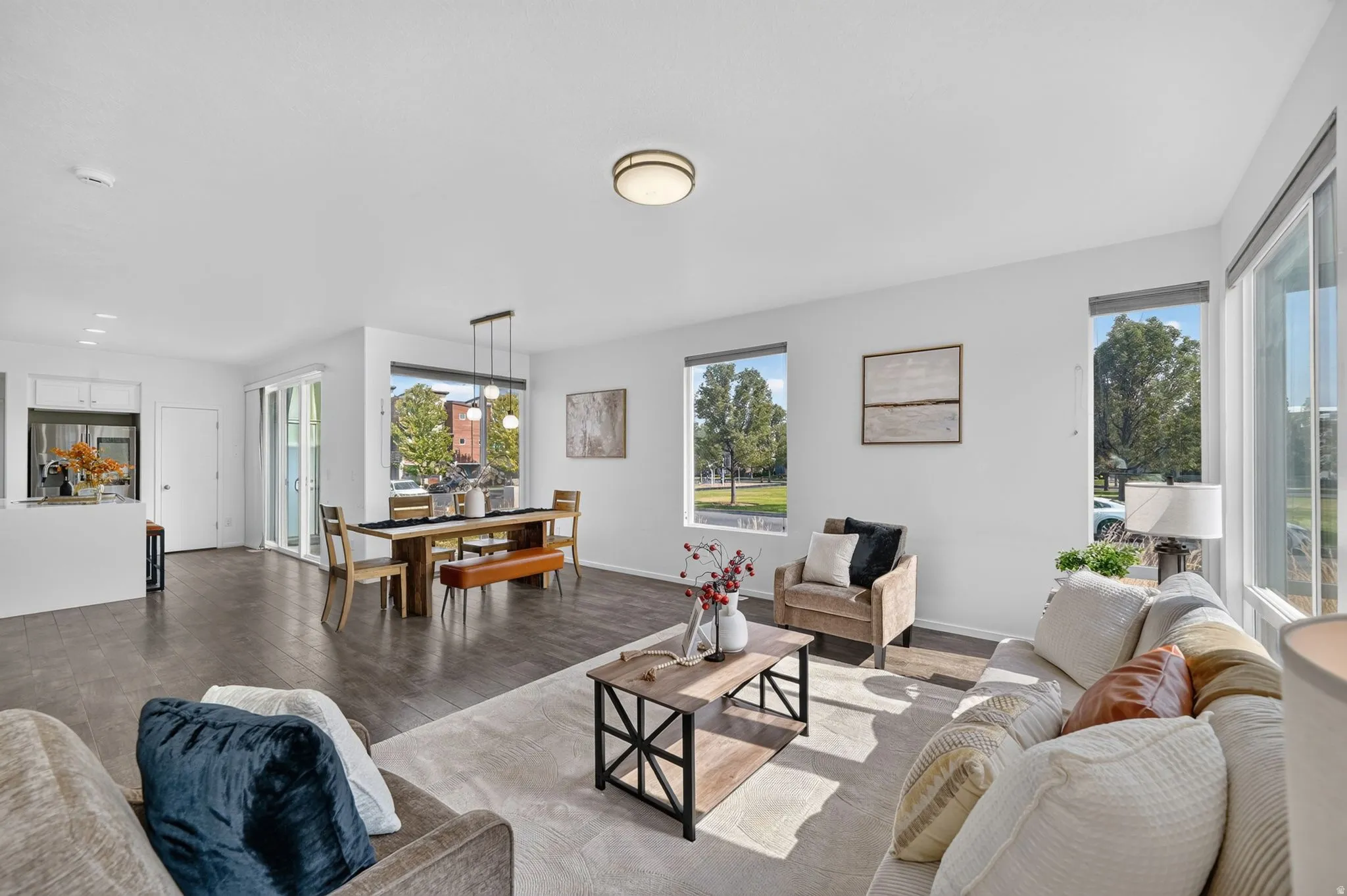 Spacious open-concept living area featuring dark wood-finish flooring, abundant natural light from multiple windows, and a modern dining area with an overhead pendant light fixture