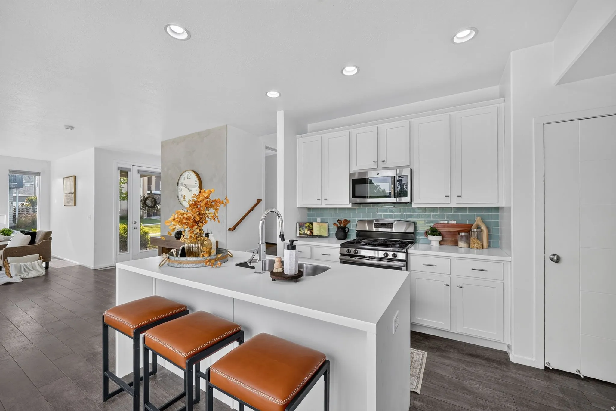 Modern kitchen featuring a central island with integrated sink, white cabinetry, stainless steel appliances, and a blue subway tile backsplash