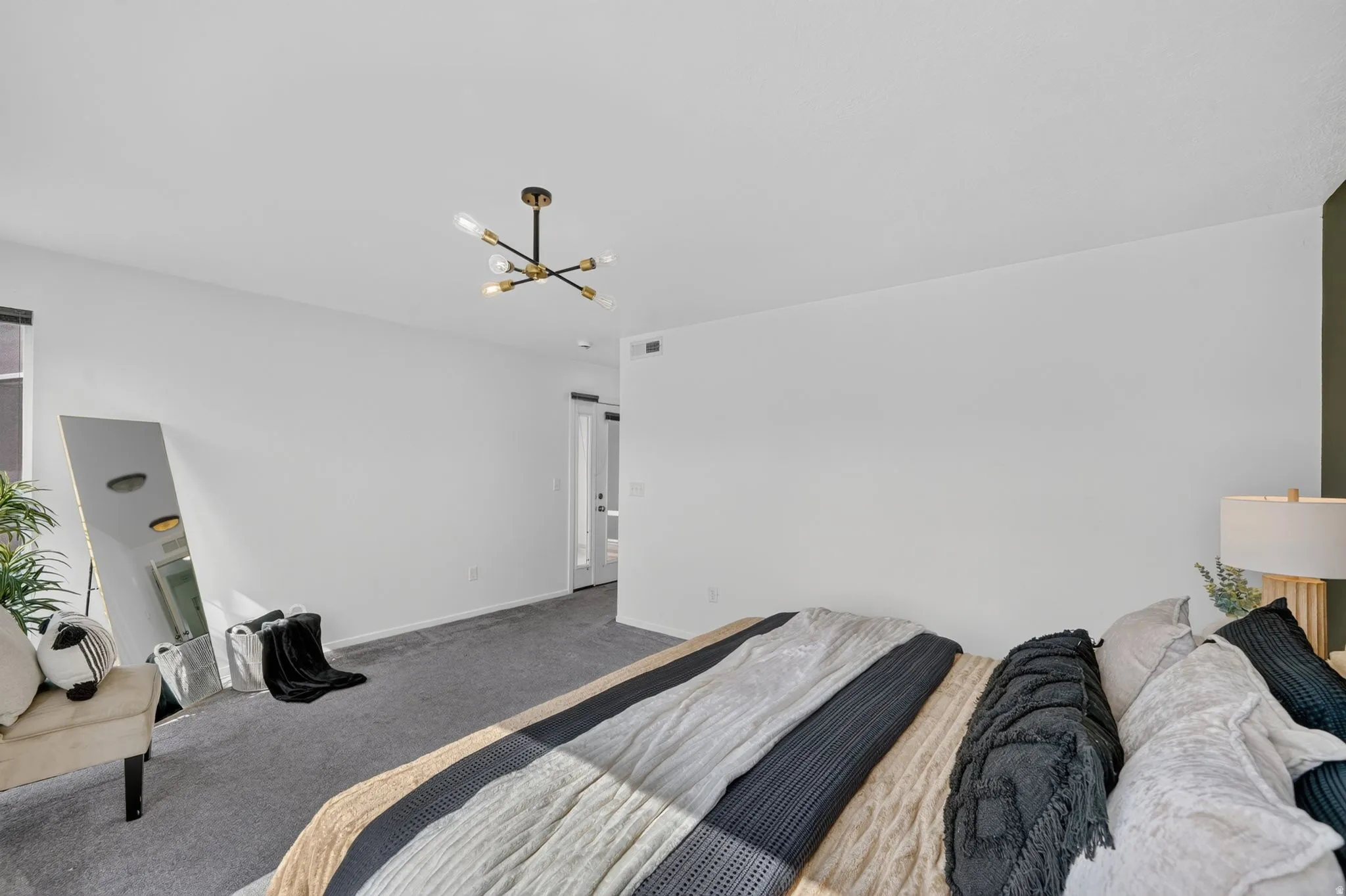 Spacious room featuring carpet flooring, white walls, and a contemporary chandelier