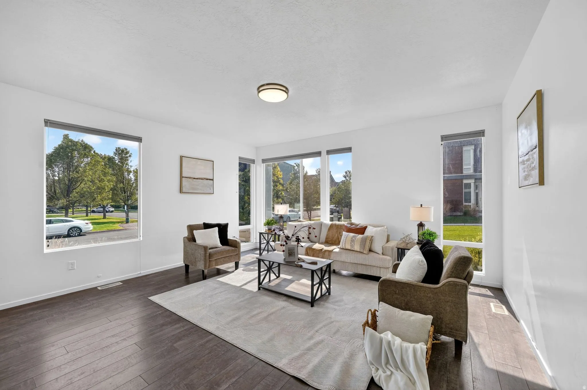 Spacious living area featuring dark wood-finish flooring, multiple large windows, and a flush-mount ceiling light