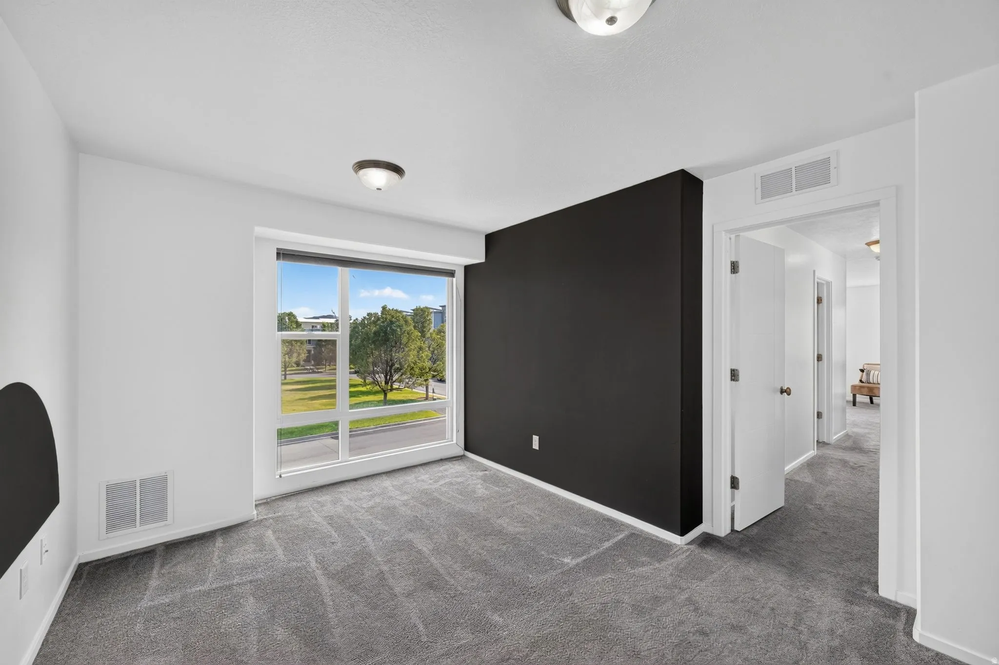 Bright interior space featuring a large window, gray carpet, a contrasting accent wall, and ceiling-mounted light fixtures