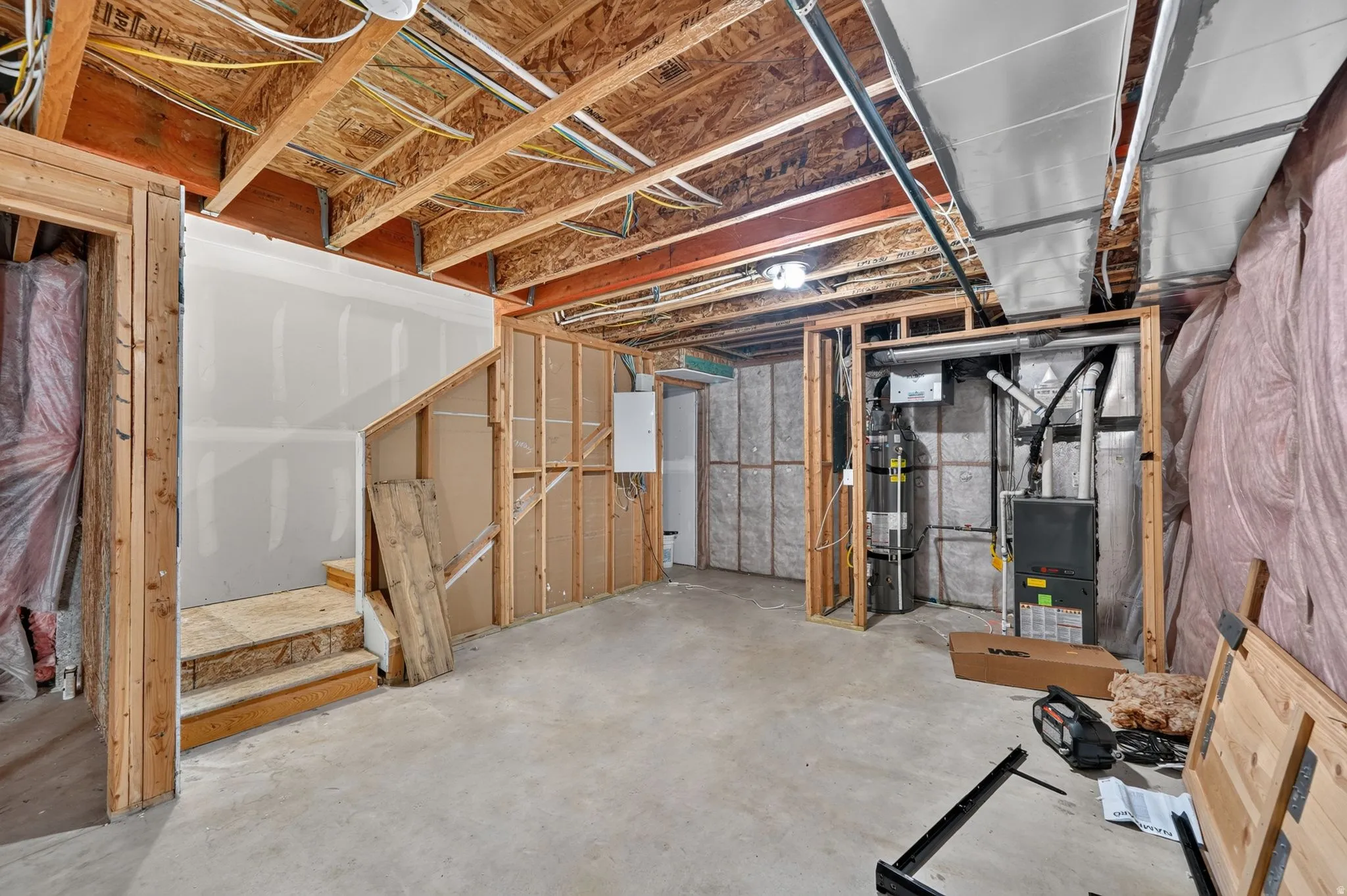 Unfinished basement space featuring exposed wood framing, concrete flooring, visible HVAC ductwork, and partially installed drywall