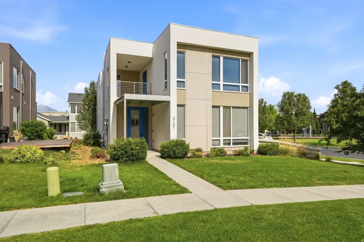 Modern architectural style with a flat roofline, multi-pane windows, a recessed entry, a second-story balcony with metal railings, and a blue entry door